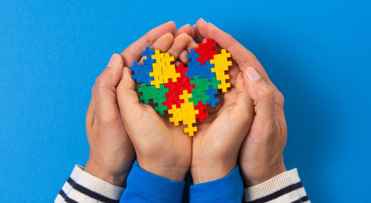 Hands holding a jigsaw puzzle coloured in various colours associated with autism awareness such as yellow, blue, red and green